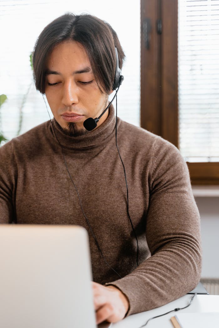 services-02 Young call center agent wearing a headset and working on a laptop in an office setting.