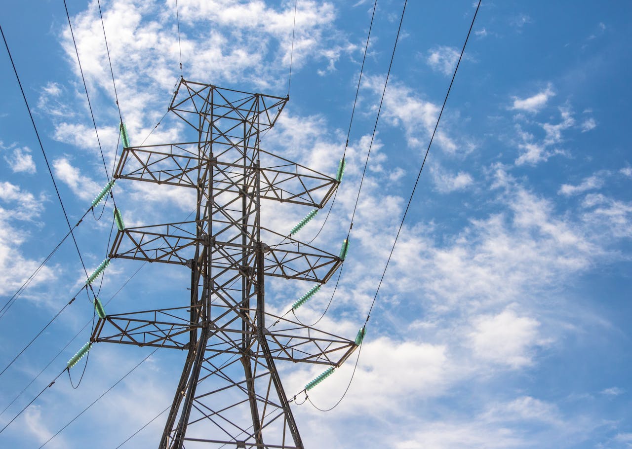 about-02 High voltage power line tower framed against a bright blue sky with clouds.